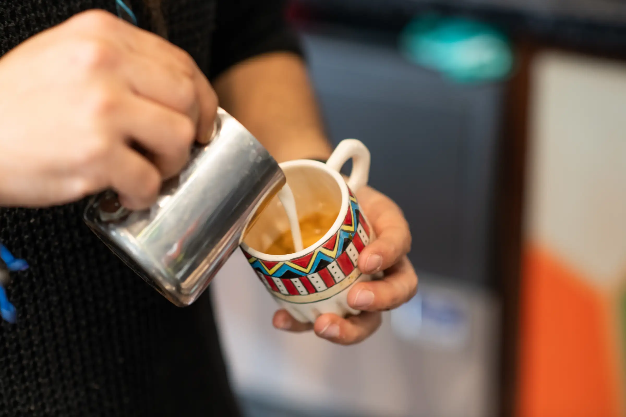 Barista pouring steamed milk into a hand painted ceramic cup