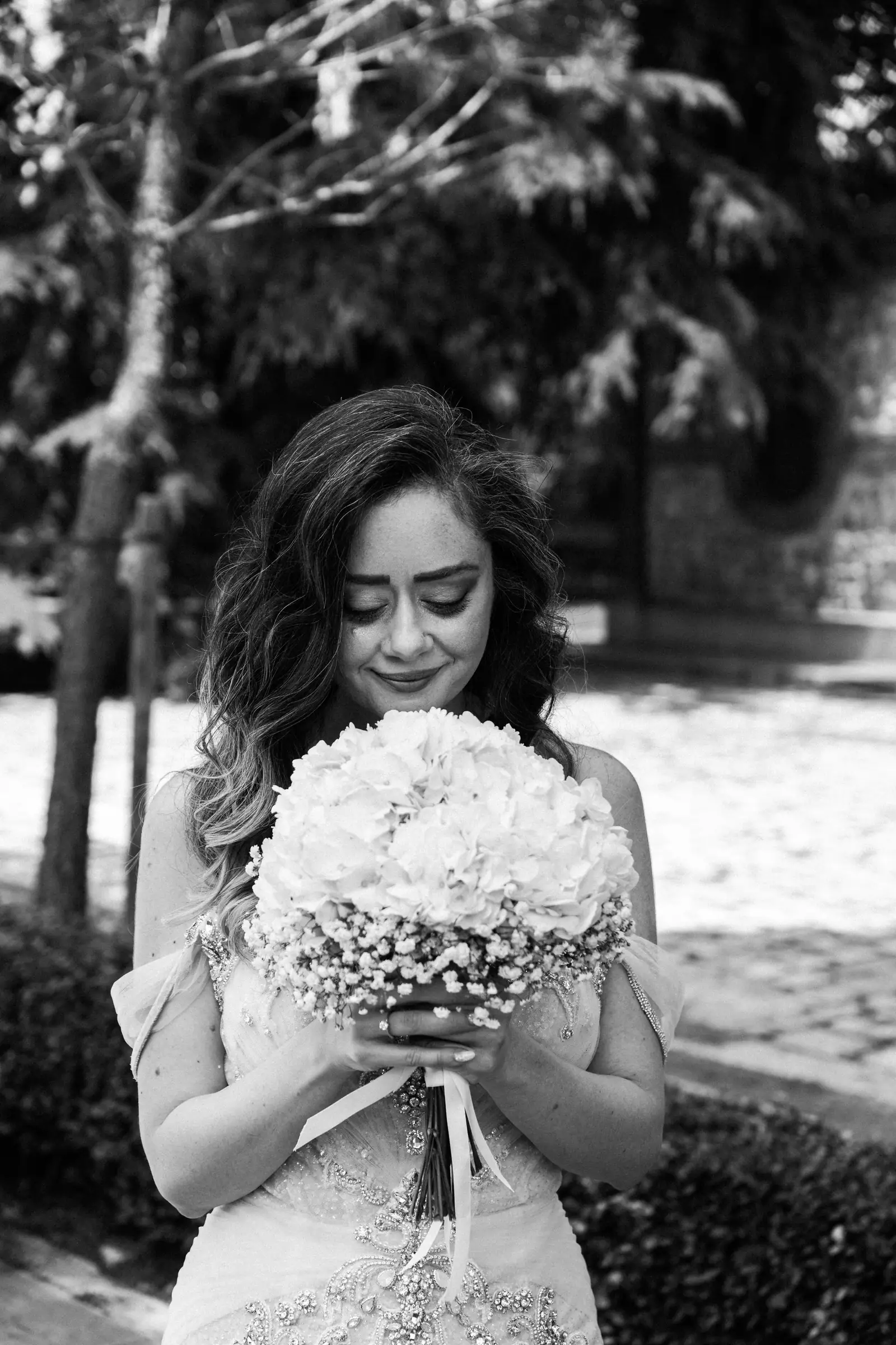 Bride looking down at her bouquet in dappled light, black and white