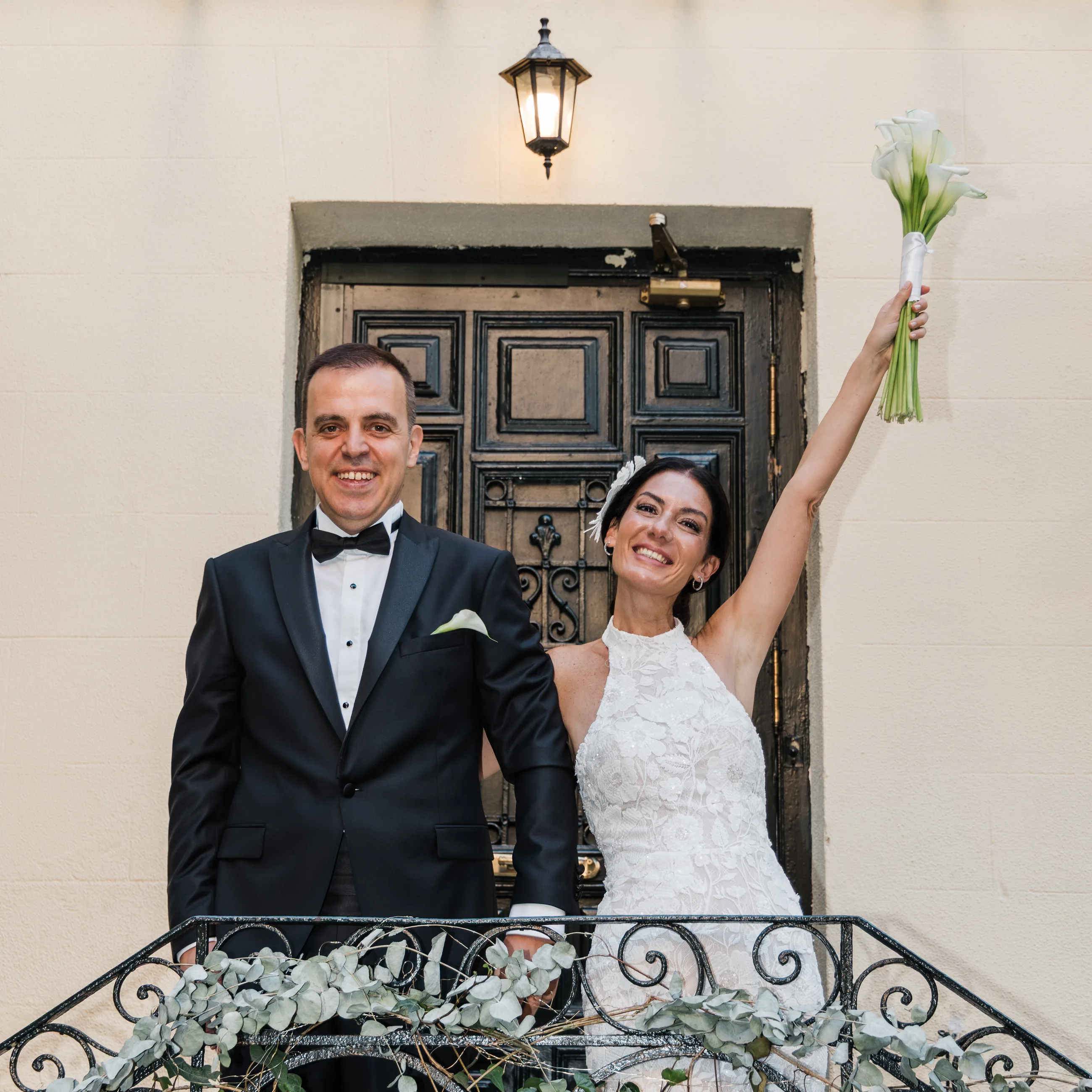 The bride raising her bouquet in front of a dark carved wooden door