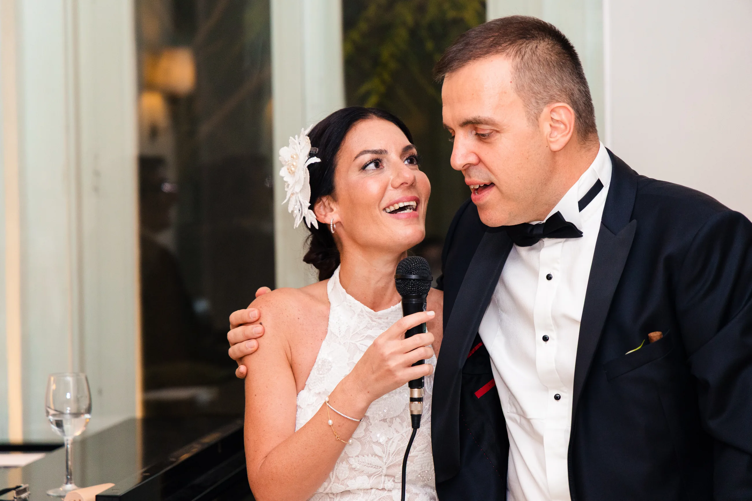 Bride singing into the microphone with the groom beside her