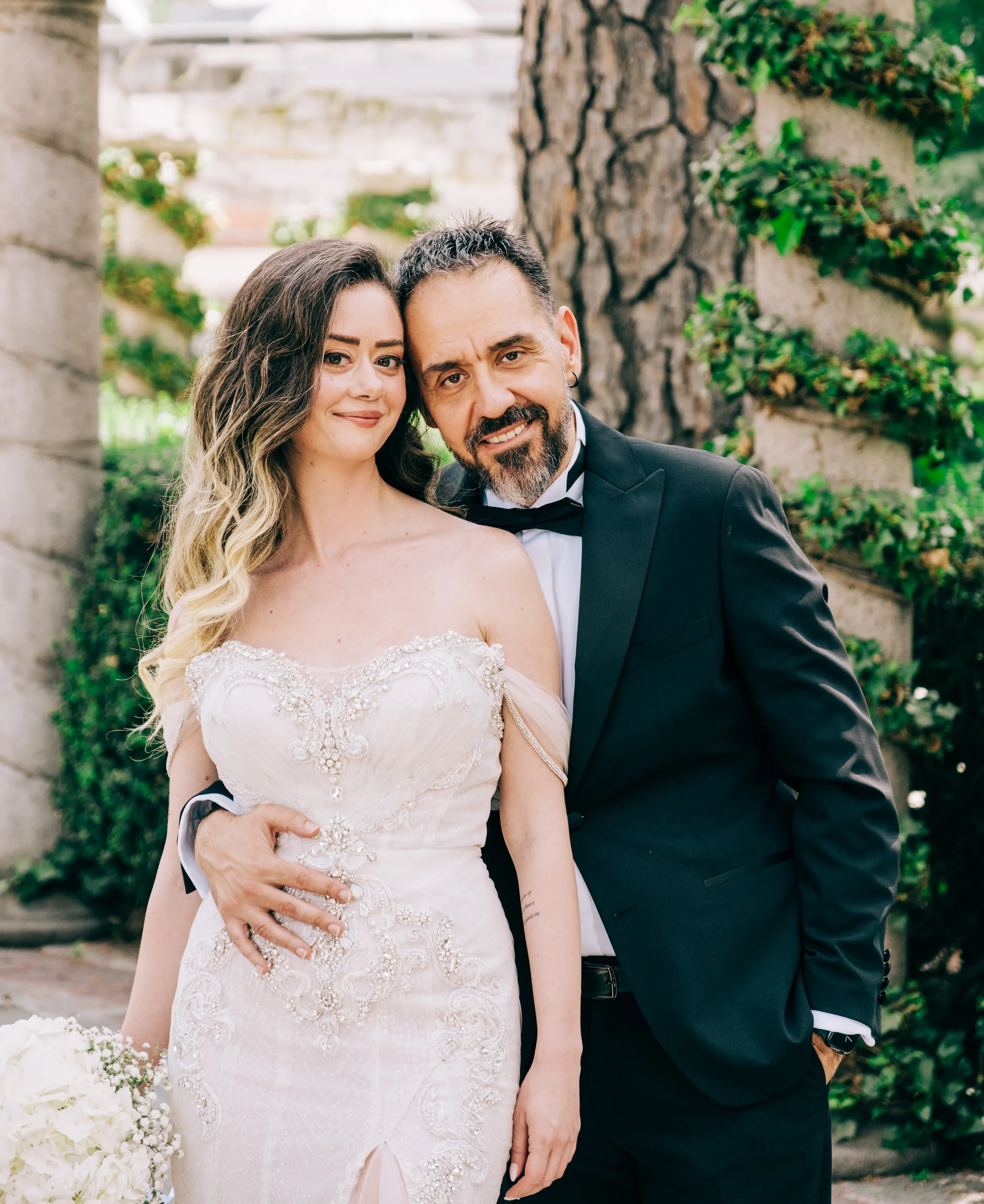 Bride and groom holding each other beside an ivy covered column in a Madrid garden