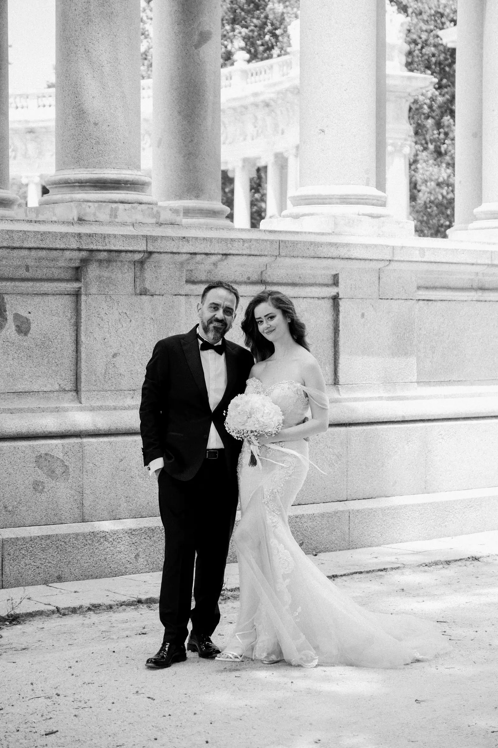 Bride and groom on the stone steps of a colonnaded monument in the Retiro, black and white