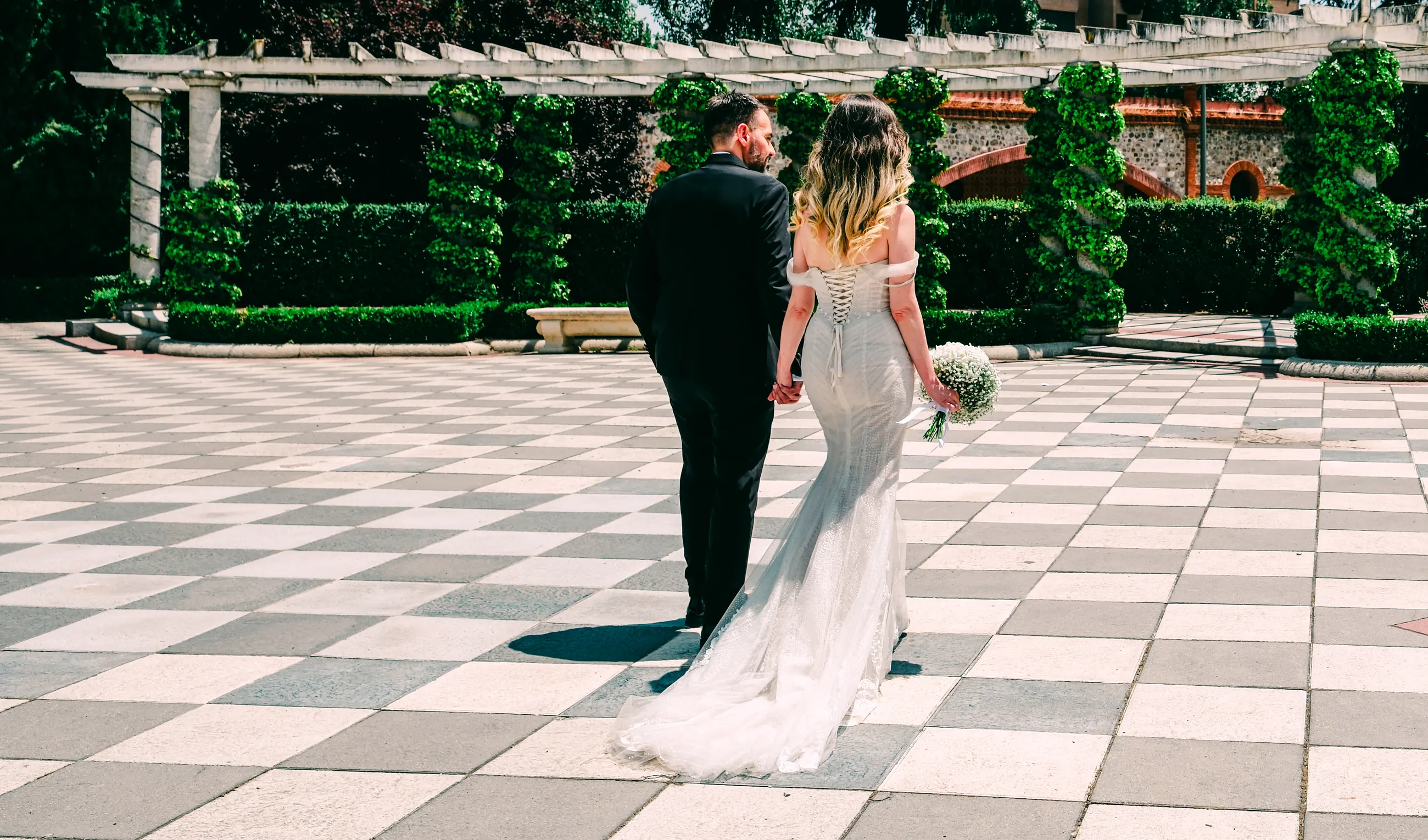 Bride and groom walking away hand in hand across a checkerboard courtyard in a Madrid garden