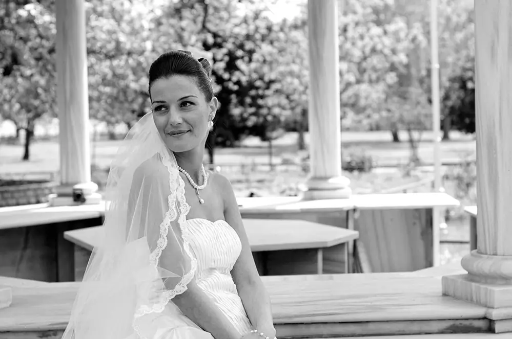 Bride seated between stone columns in her veil, black and white
