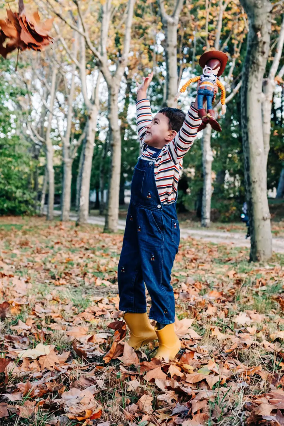 Boy holding his toy up towards the autumn trees