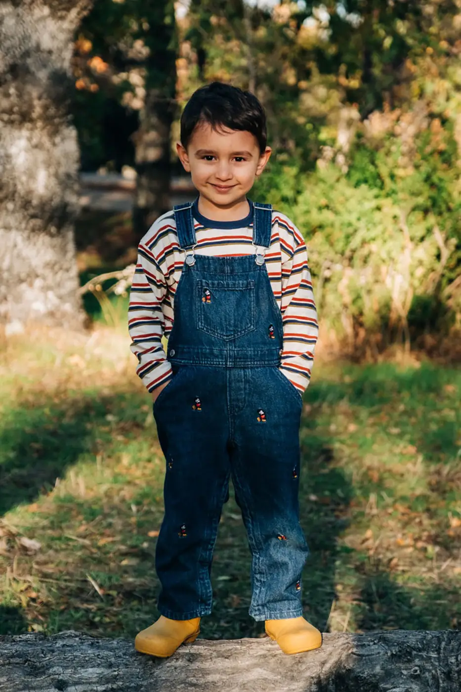 Young boy in dungarees standing on a park path in autumn