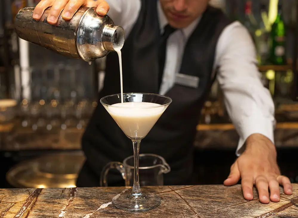 Bartender pouring a cocktail from a shaker into a coupe glass