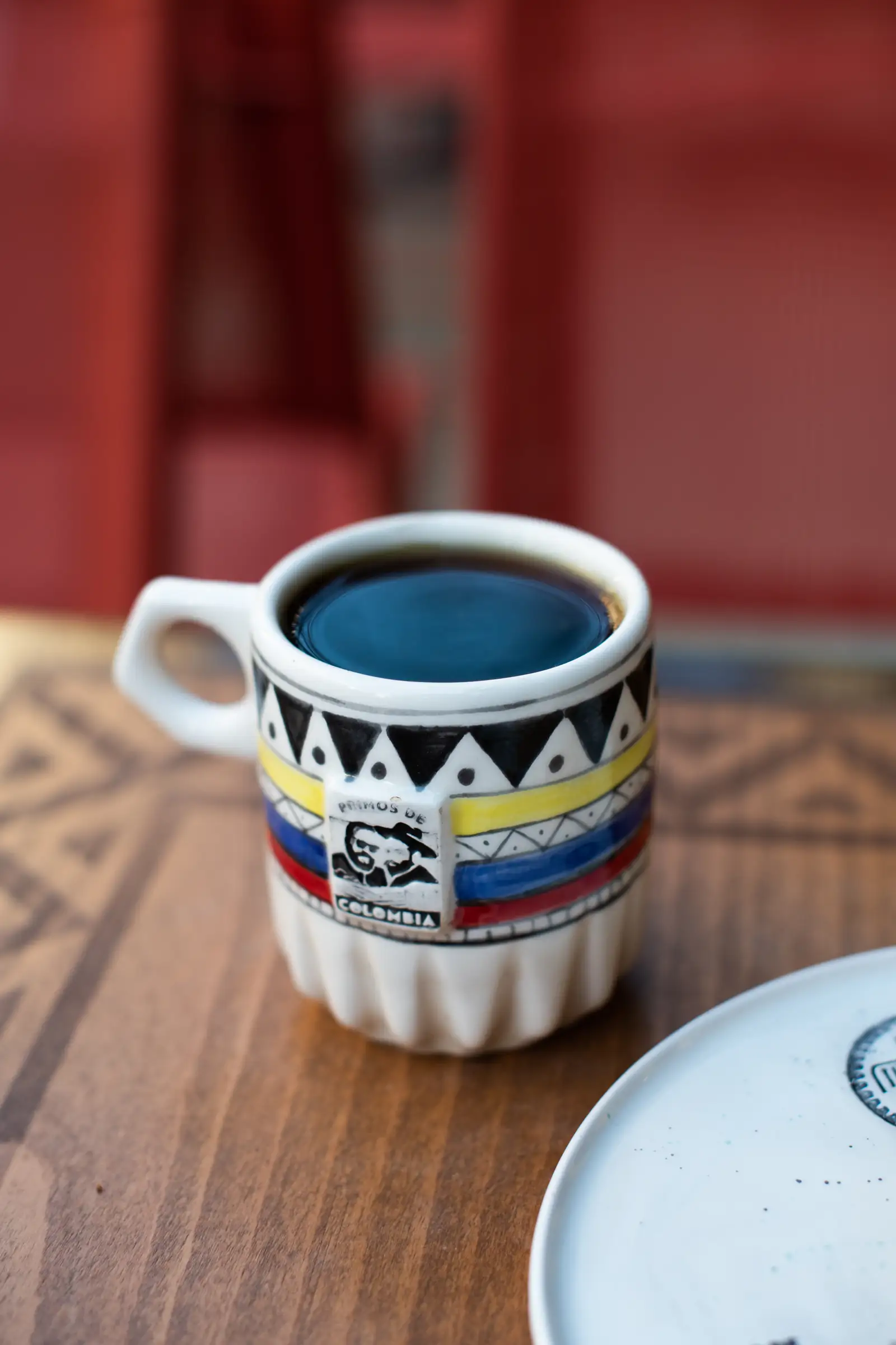 Ceramic cup in Colombian flag colours filled with black coffee on a wooden table