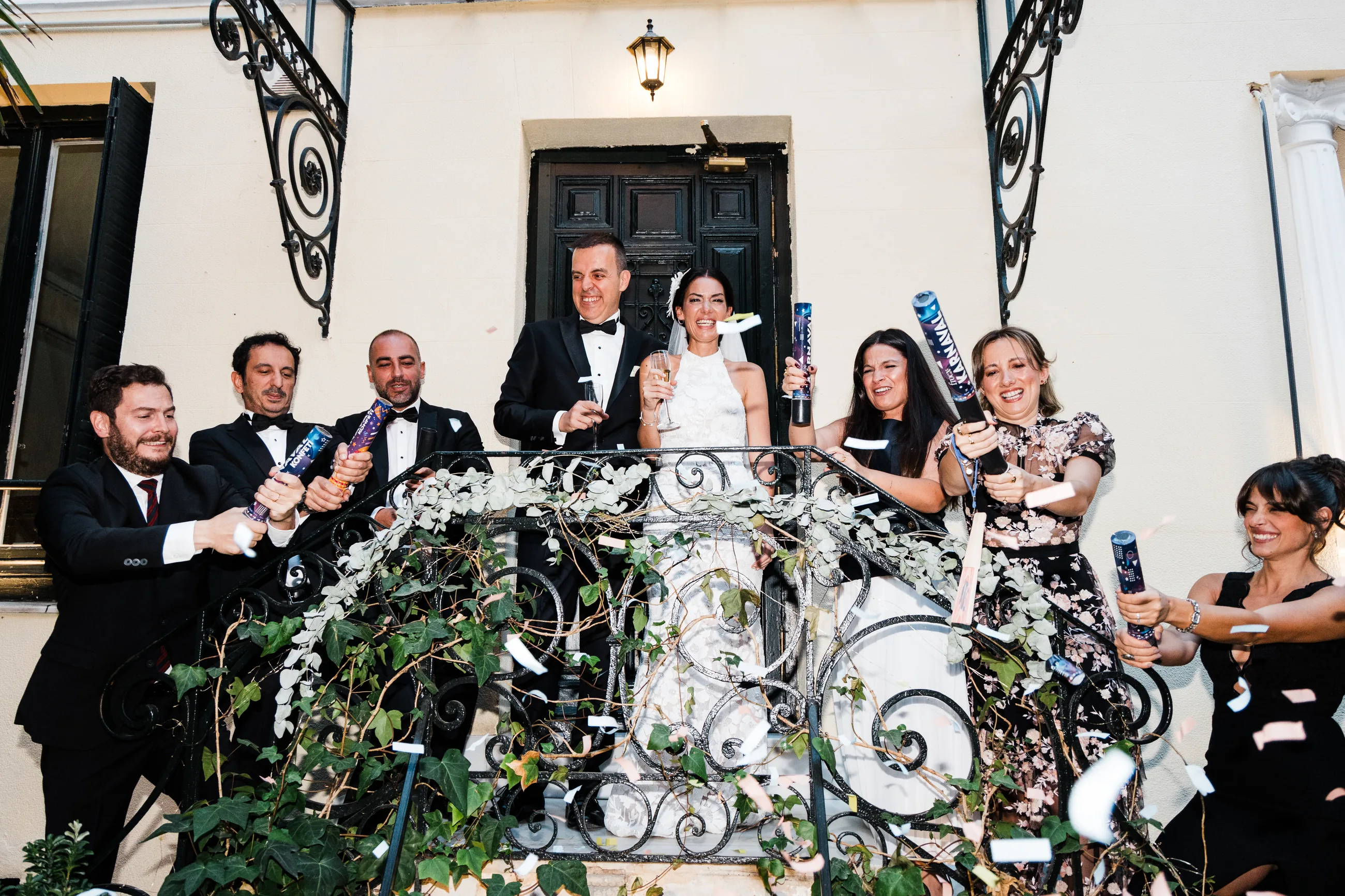 Friends firing confetti around the couple on a garden balcony