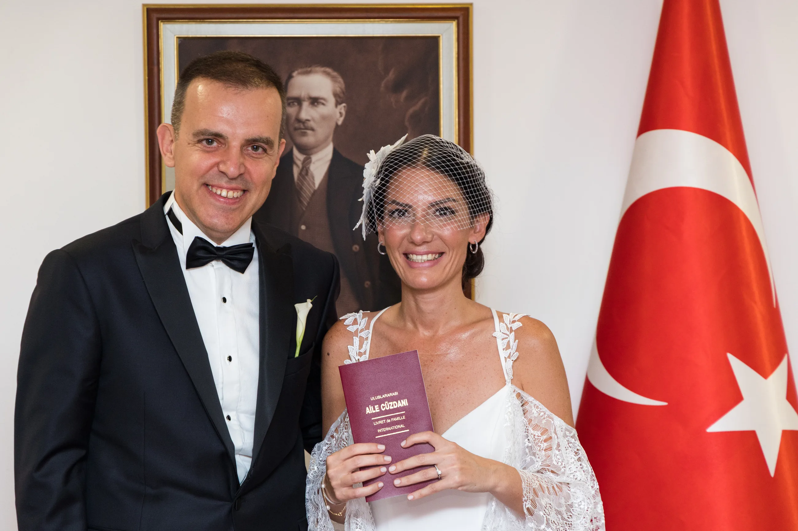 The bride and the groom smiling outside the consulate with the red family booklet