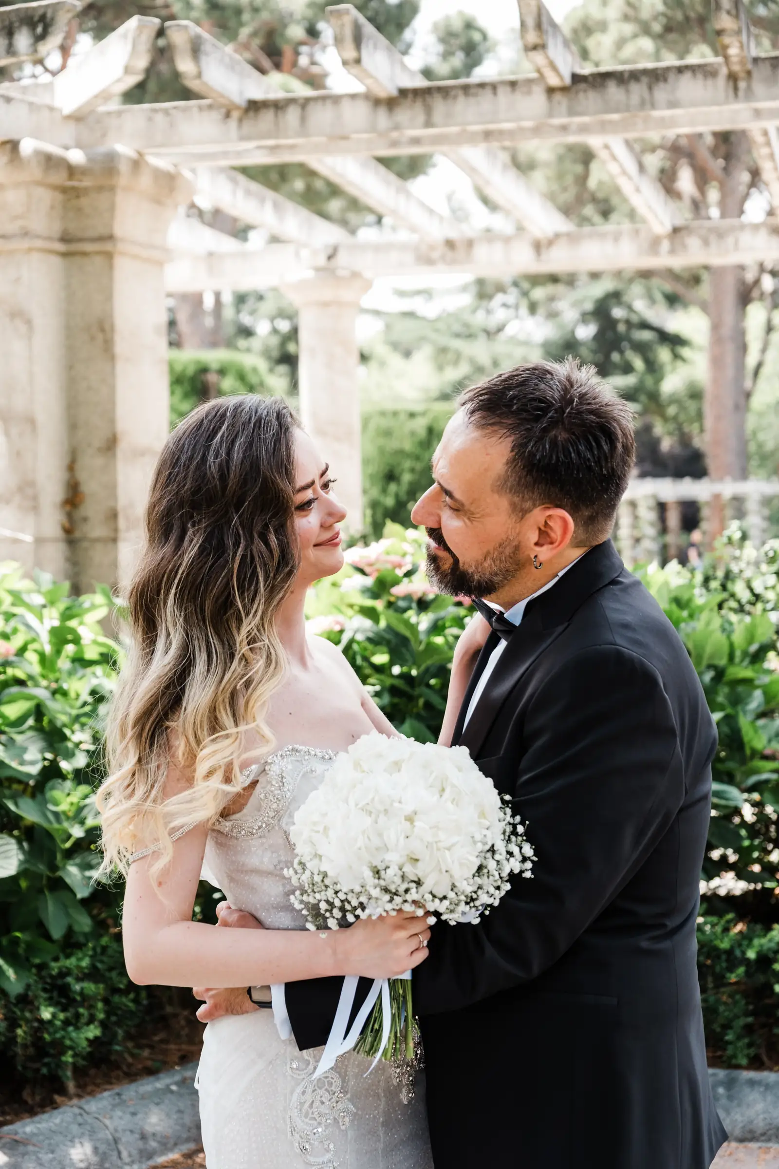 Couple standing forehead to forehead with a white bouquet in a Madrid garden