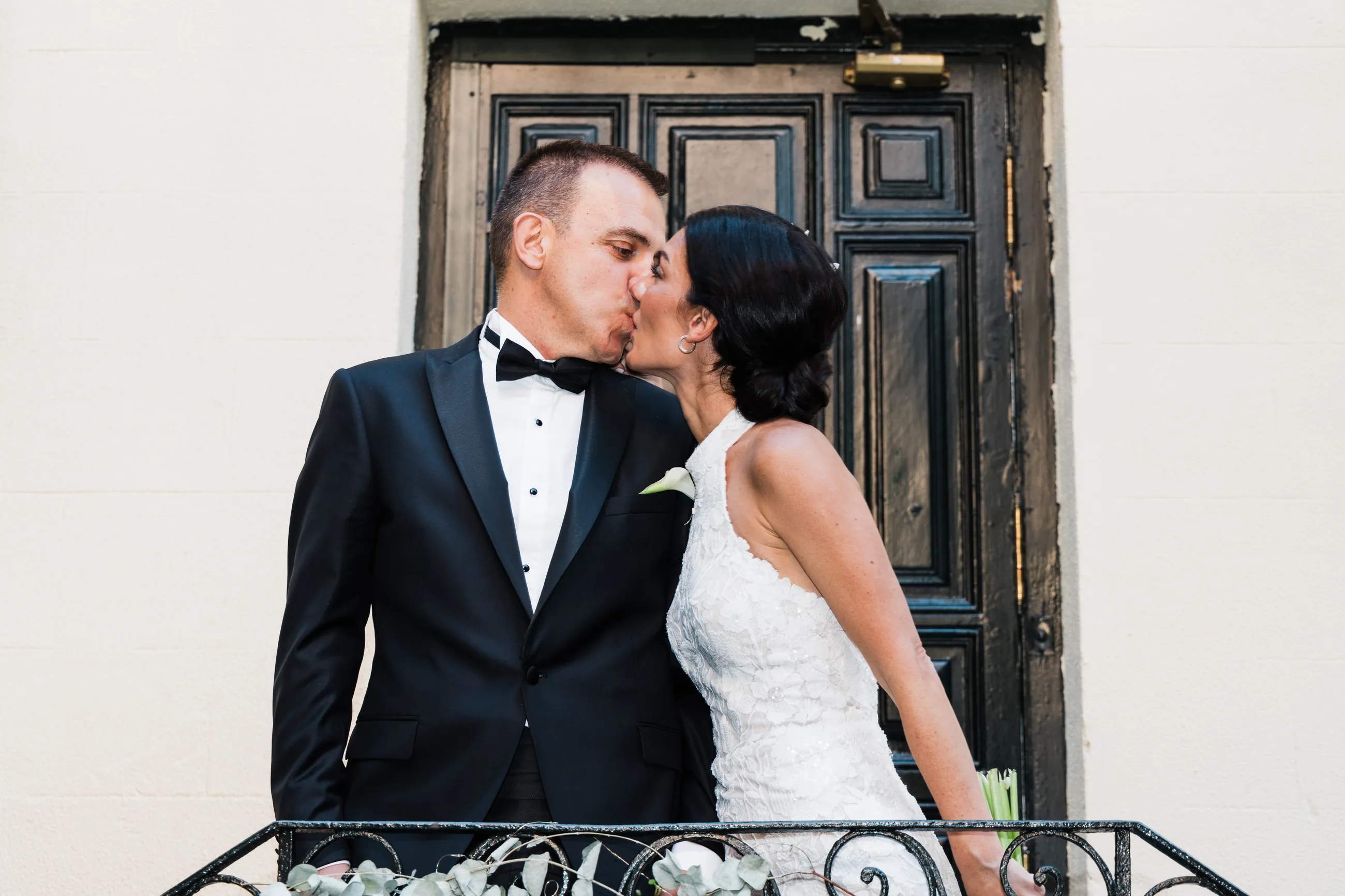 Couple kissing on a balcony in front of a dark wooden door