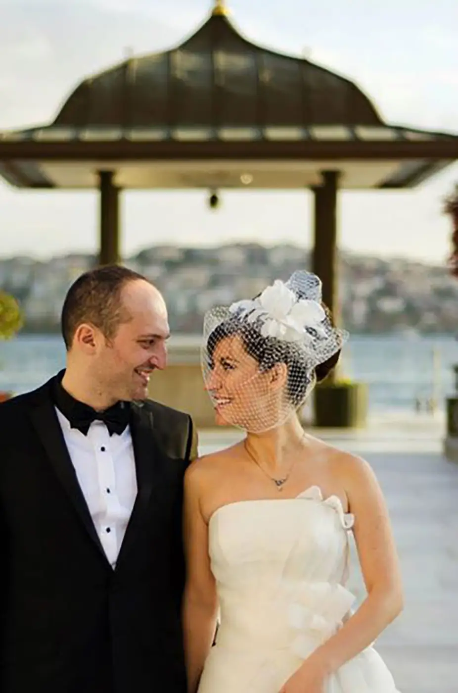 Bride and groom under a waterside pavilion looking at each other