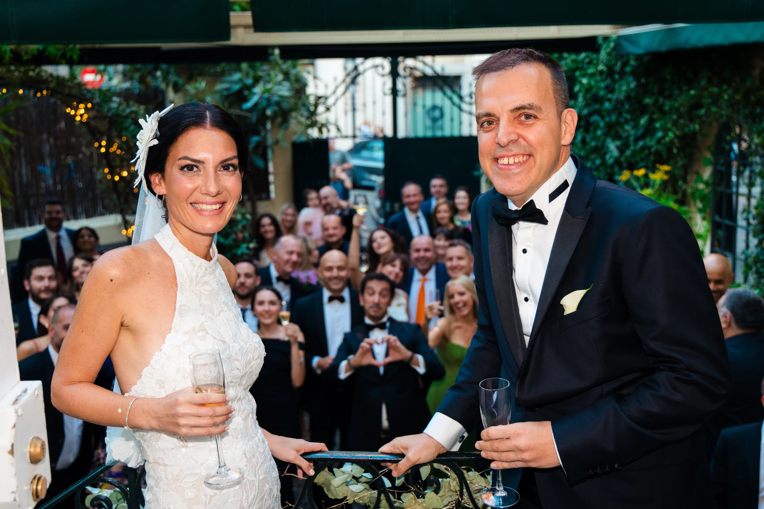 Bride and groom raising a glass with their guests gathered behind them