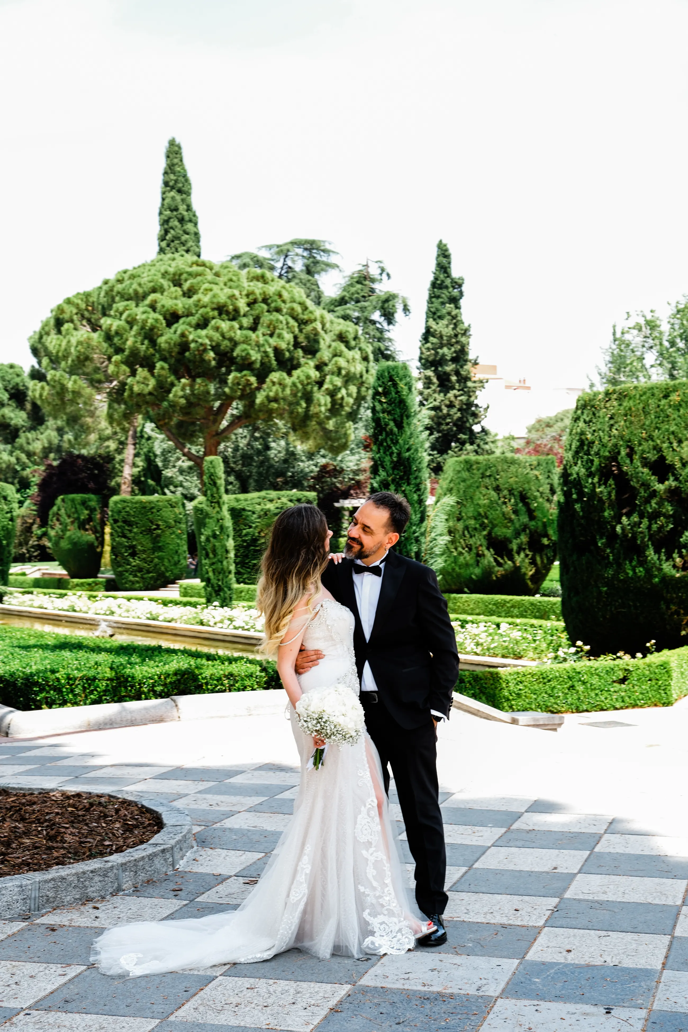 Couple standing together among clipped topiary and stone pines in Madrid