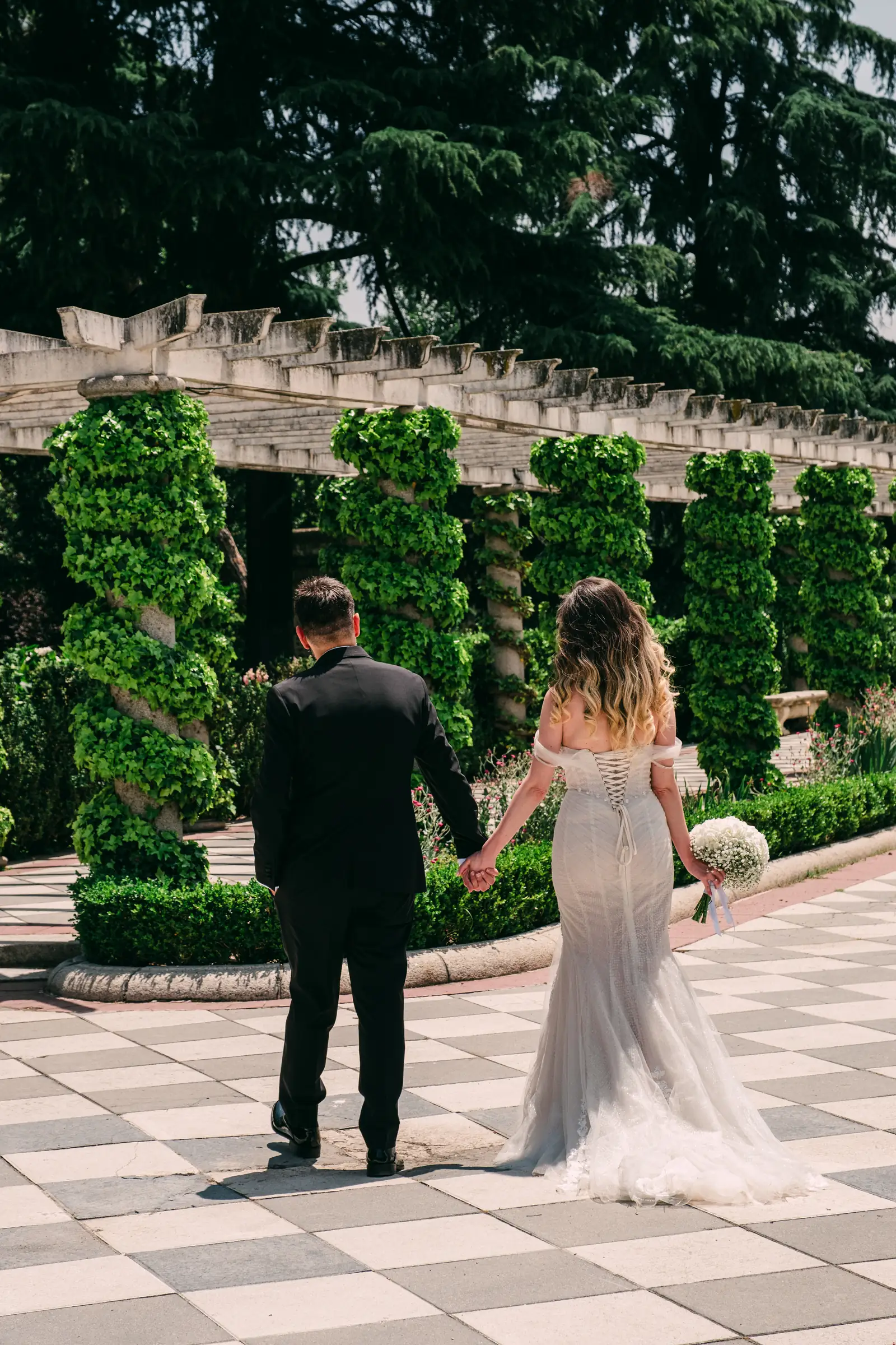 Couple walking away hand in hand along a pergola path in Madrid