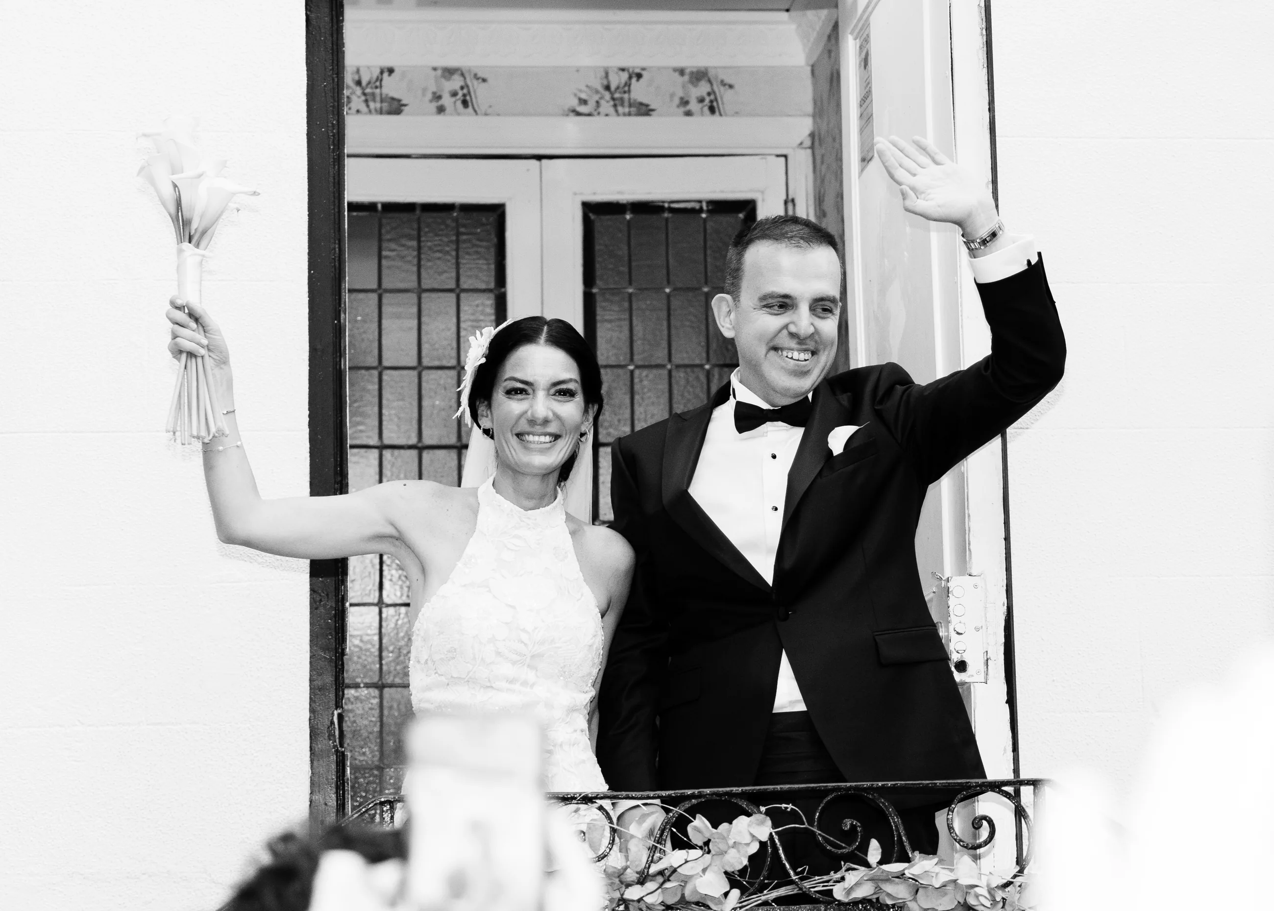 Black and white: the bride and the groom waving from the balcony to the garden