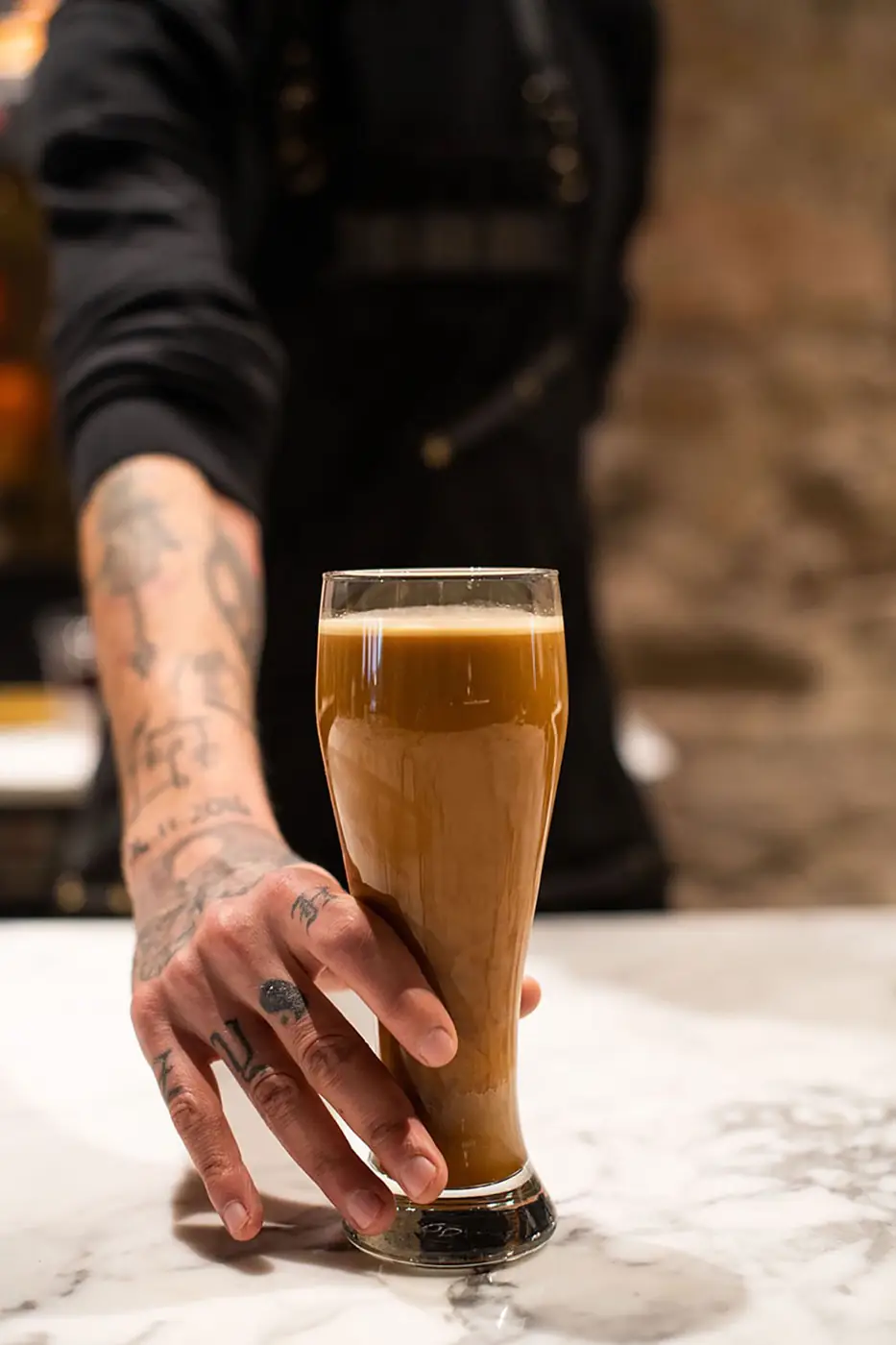 Bartender placing a tall glass of coffee stout on a marble counter
