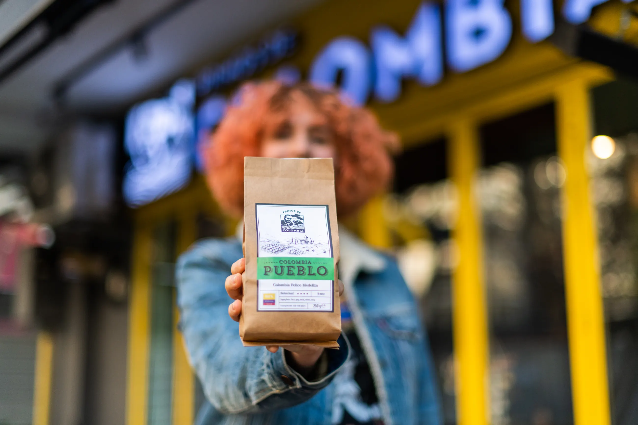 Customer holding a bag of coffee out to the camera in front of the shop