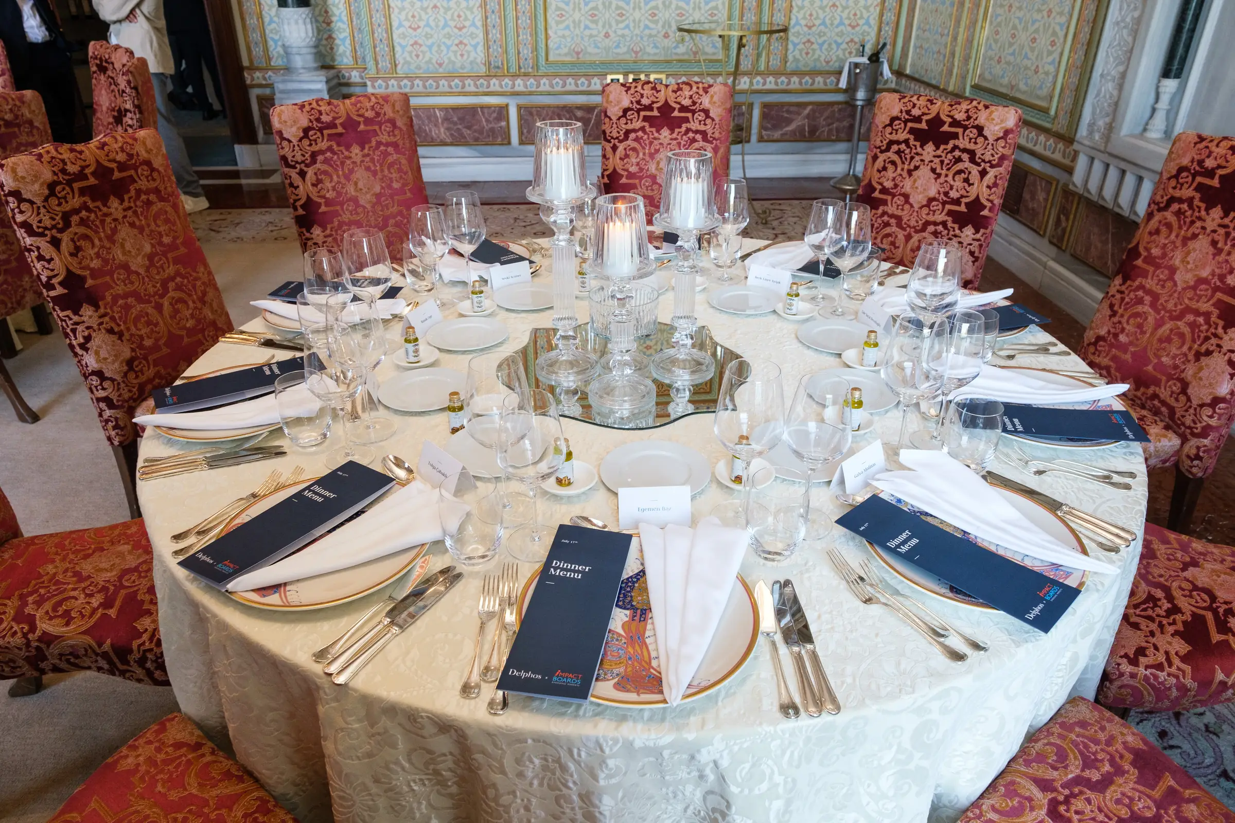 Round table laid with glassware, candles and printed menus before a formal dinner