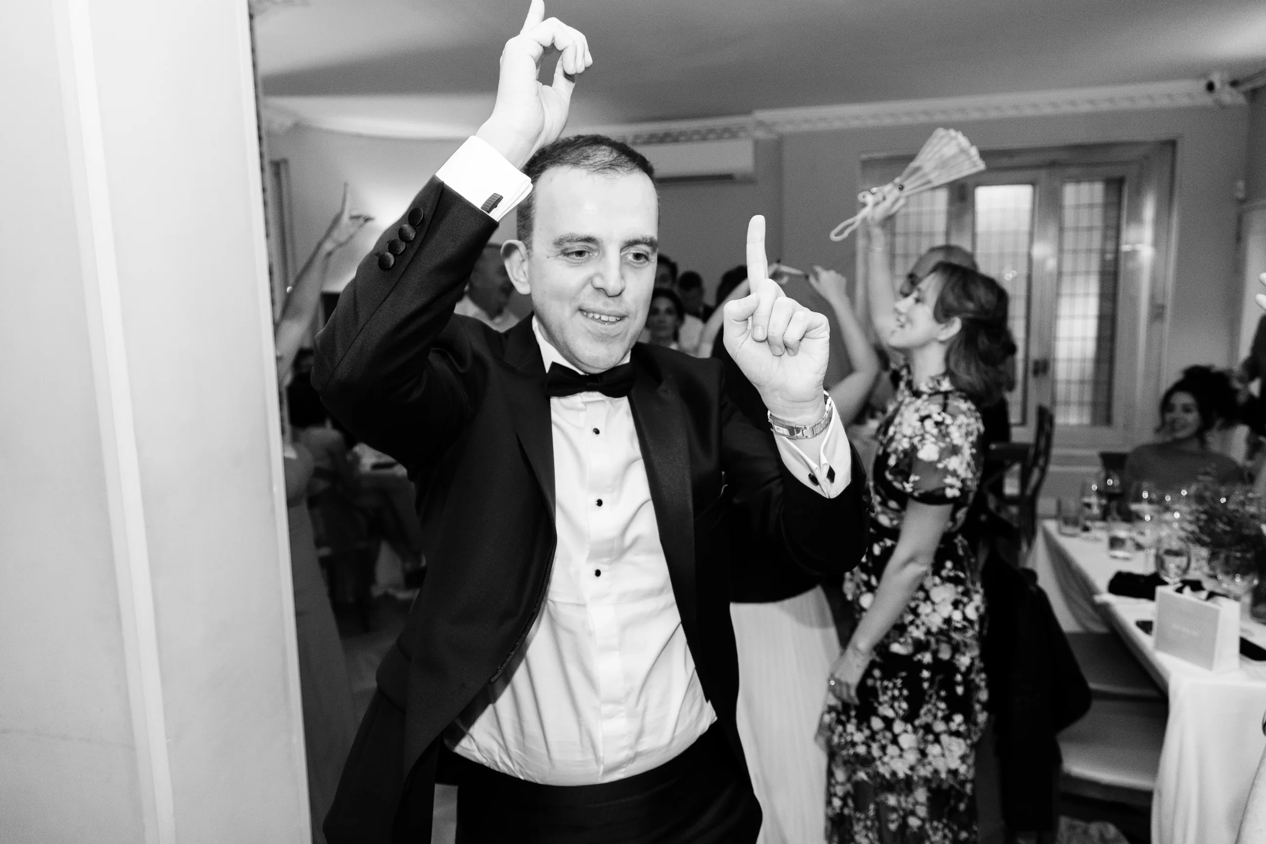 Groom dancing with his hands in the air at the party, black and white