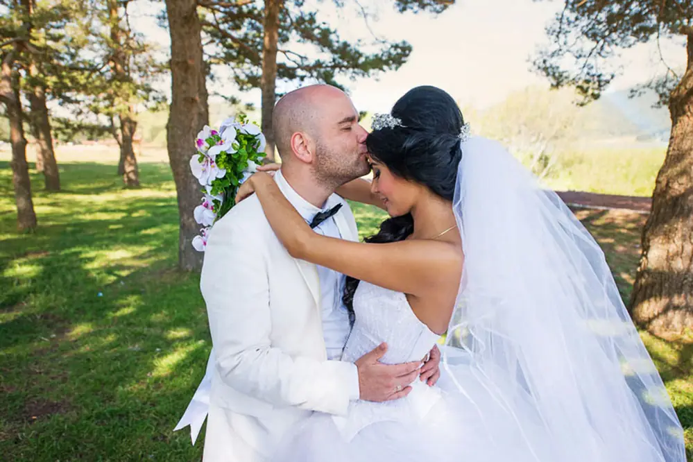 Groom kissing the bride on the forehead among pine trees