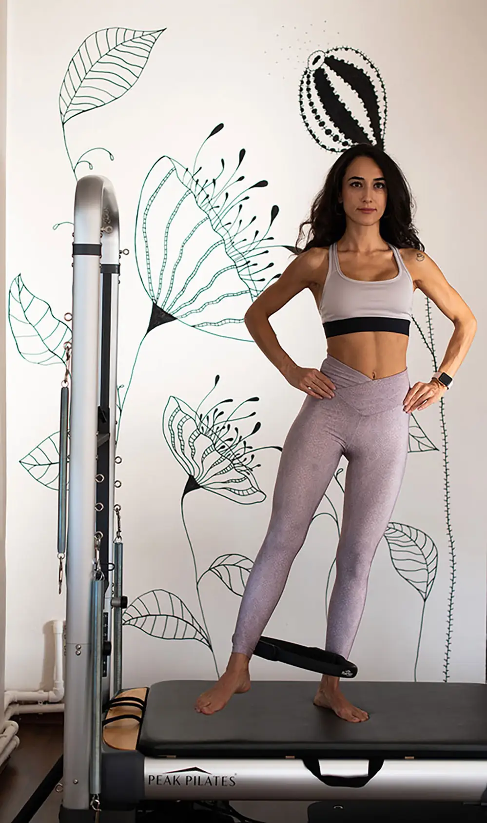 Instructor standing with hands on hips in front of a painted floral wall