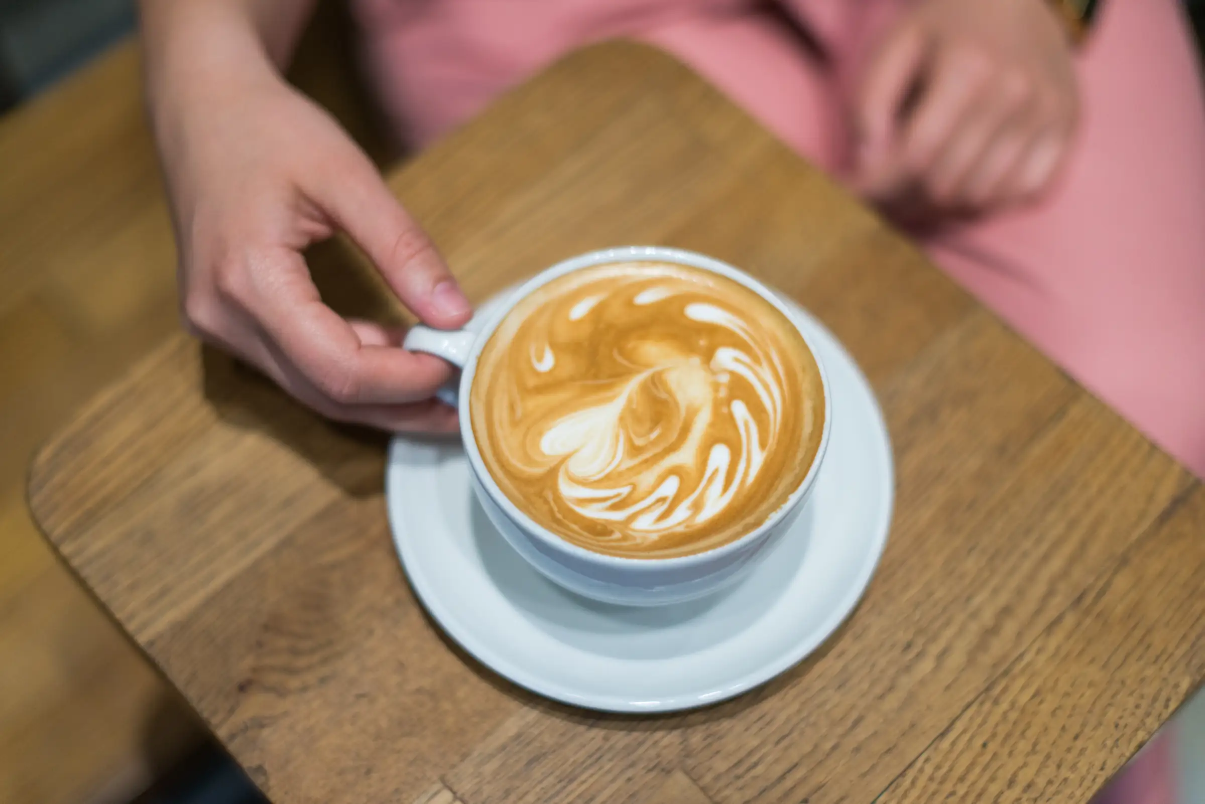 Cappuccino with latte art on a wooden table, seen from above as it is served