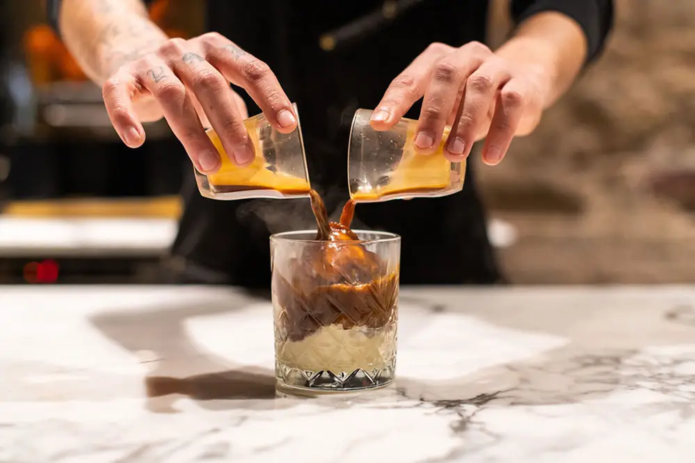 Two hands pouring a layered iced coffee into a glass