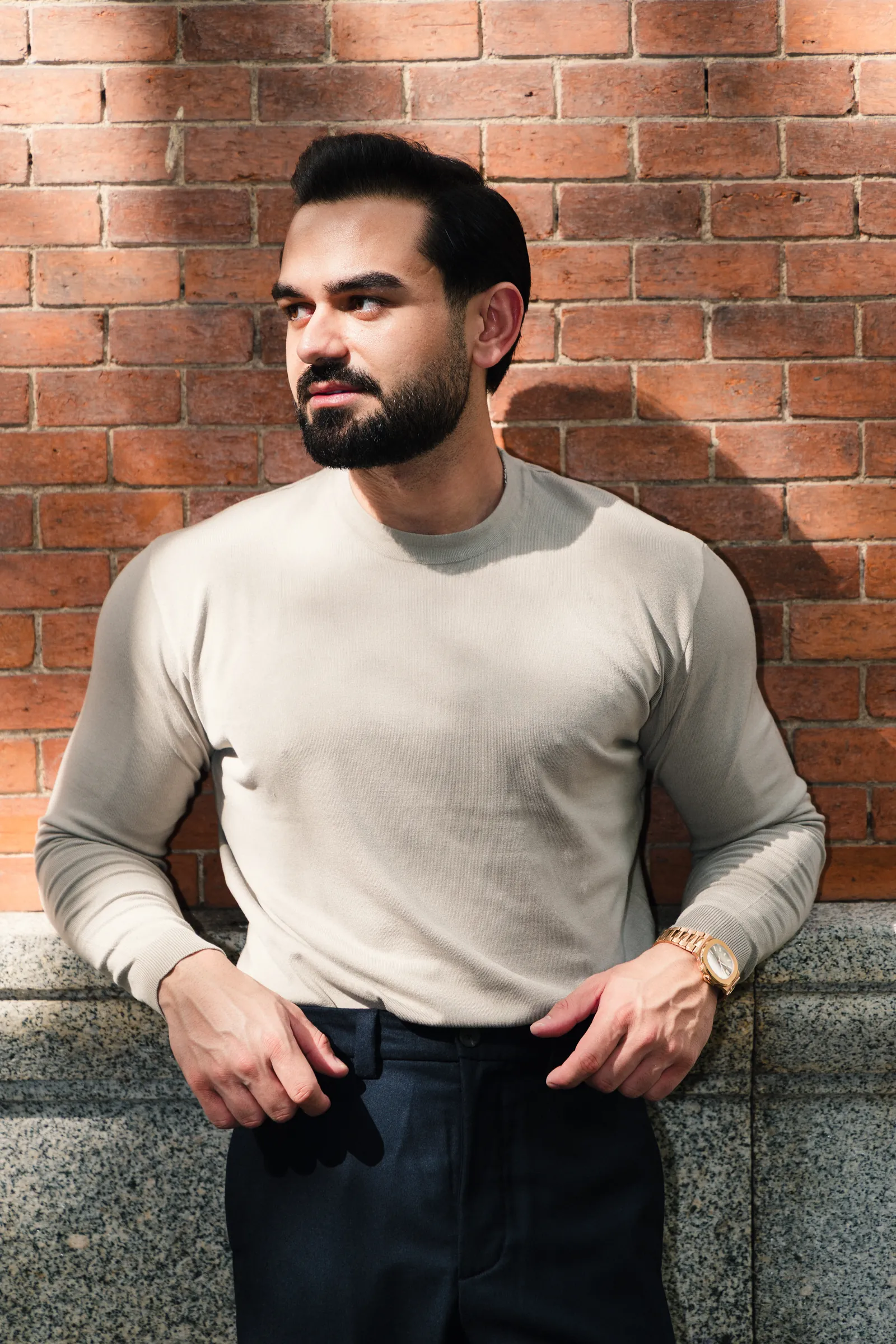Close portrait of a man in a light knit leaning on a red brick wall
