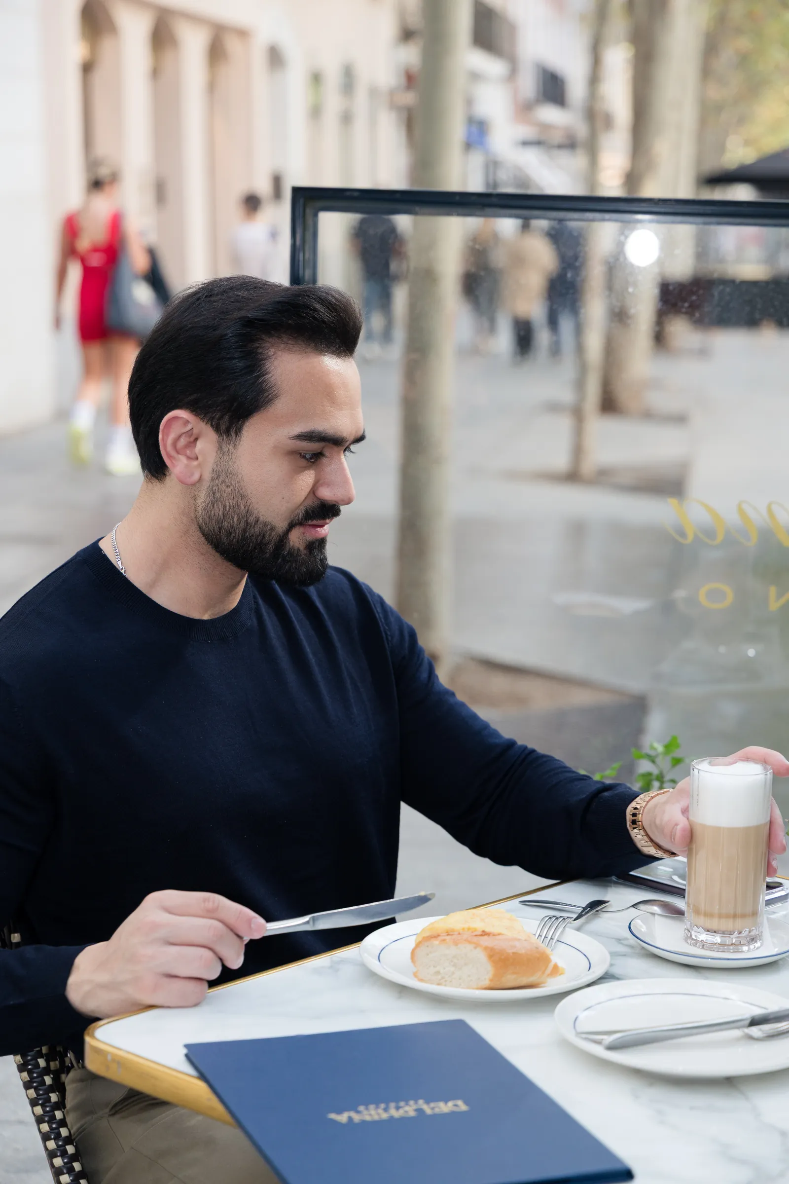 Man in a navy knit at a café terrace table with a coffee