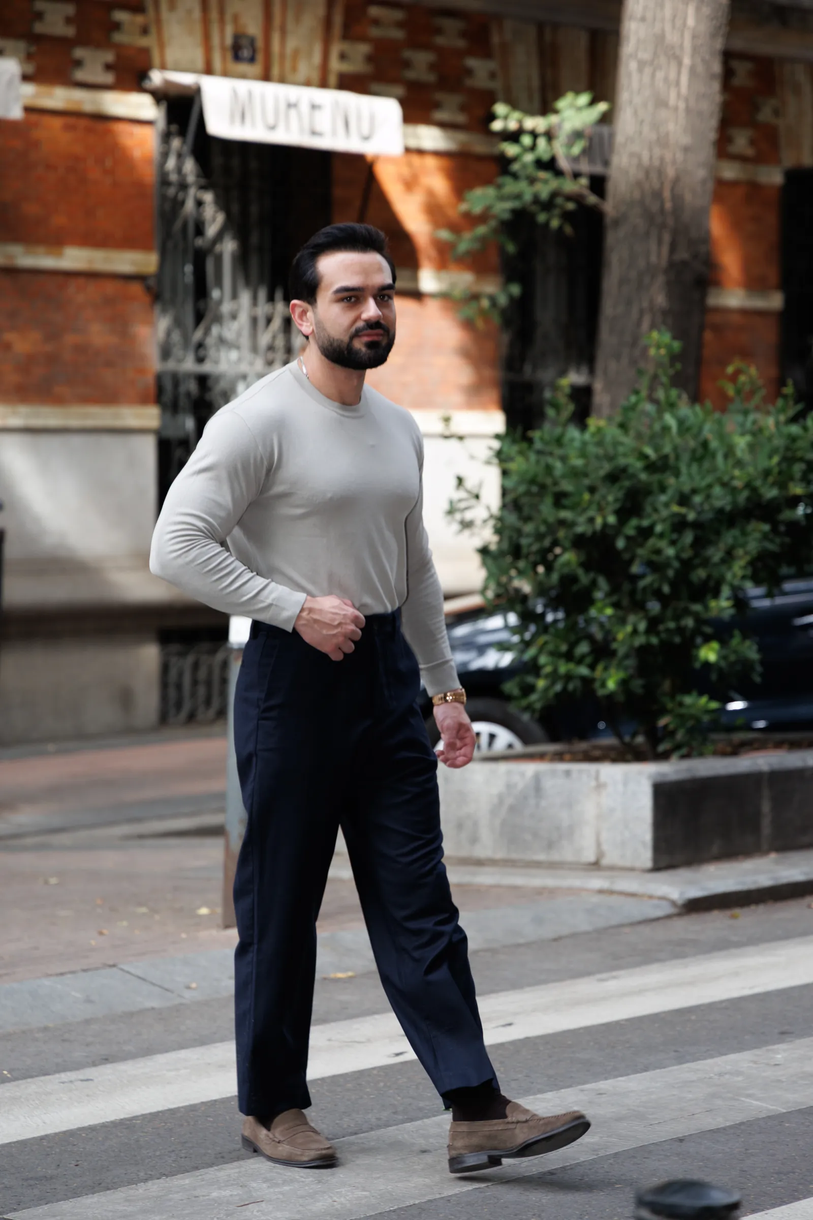 Man in a light knit and navy trousers crossing a quiet side street