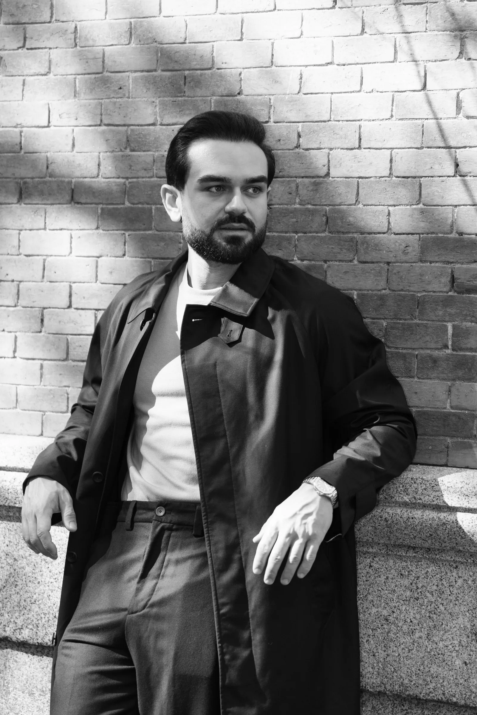 Black and white: man in a dark coat leaning against a white brick wall