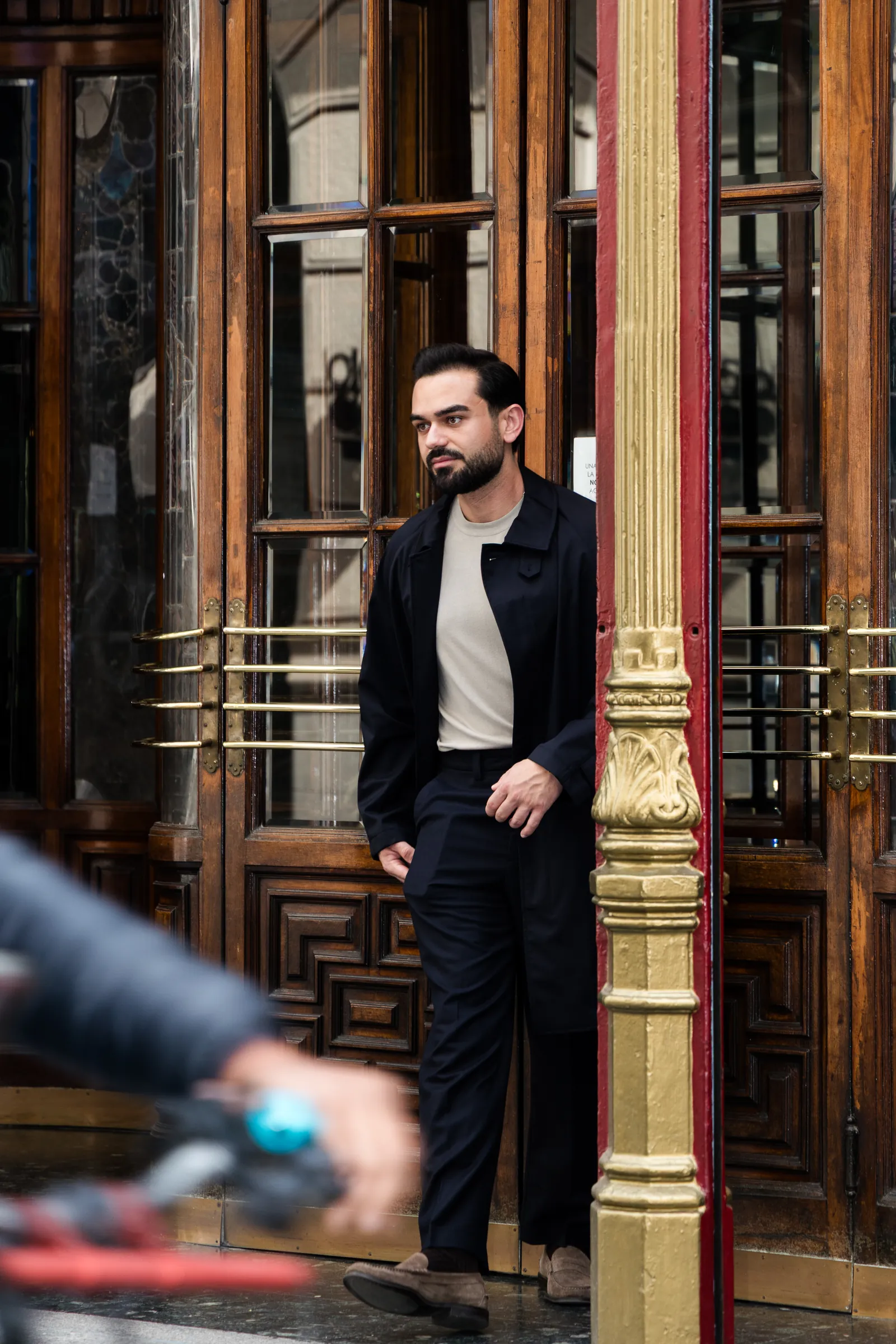 Man in a navy coat stepping out of carved wooden theatre doors as a cyclist passes