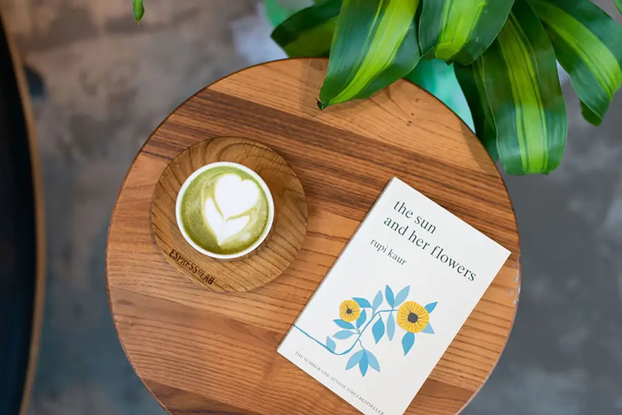 Cup of matcha on a wooden board beside a printed card and a plant, seen from above