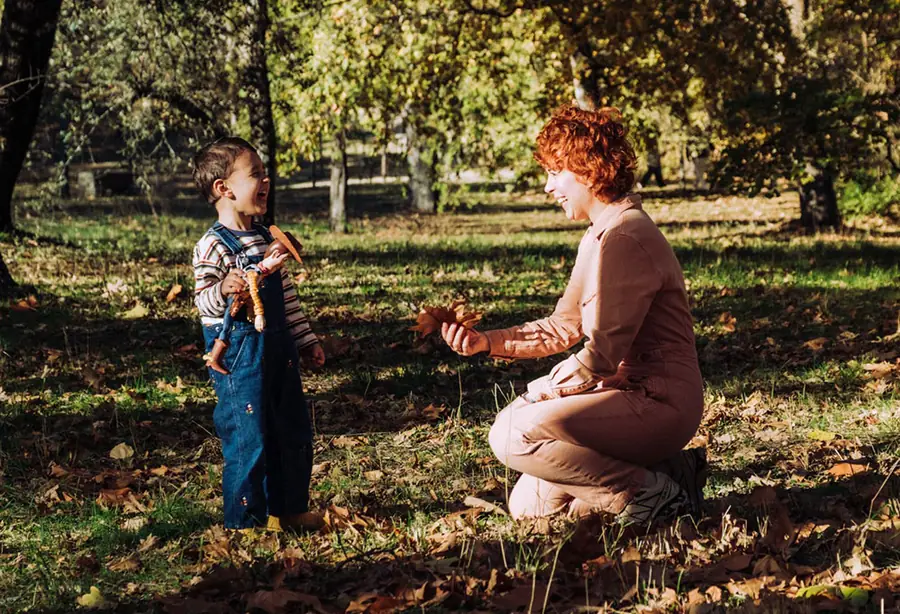 Mother crouching next to her son among autumn leaves in a park