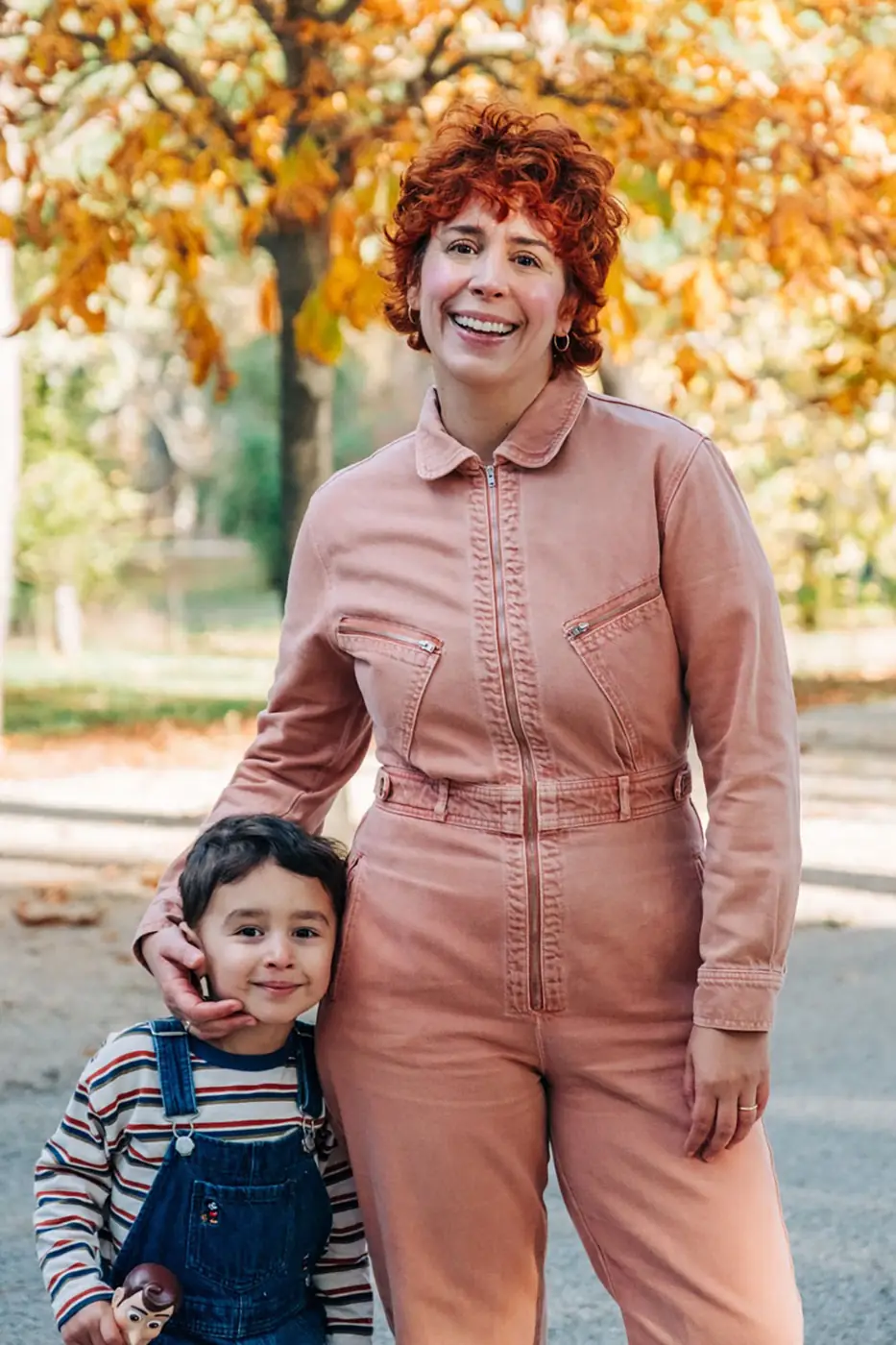 Mother in a pink jumpsuit standing with her son under autumn trees