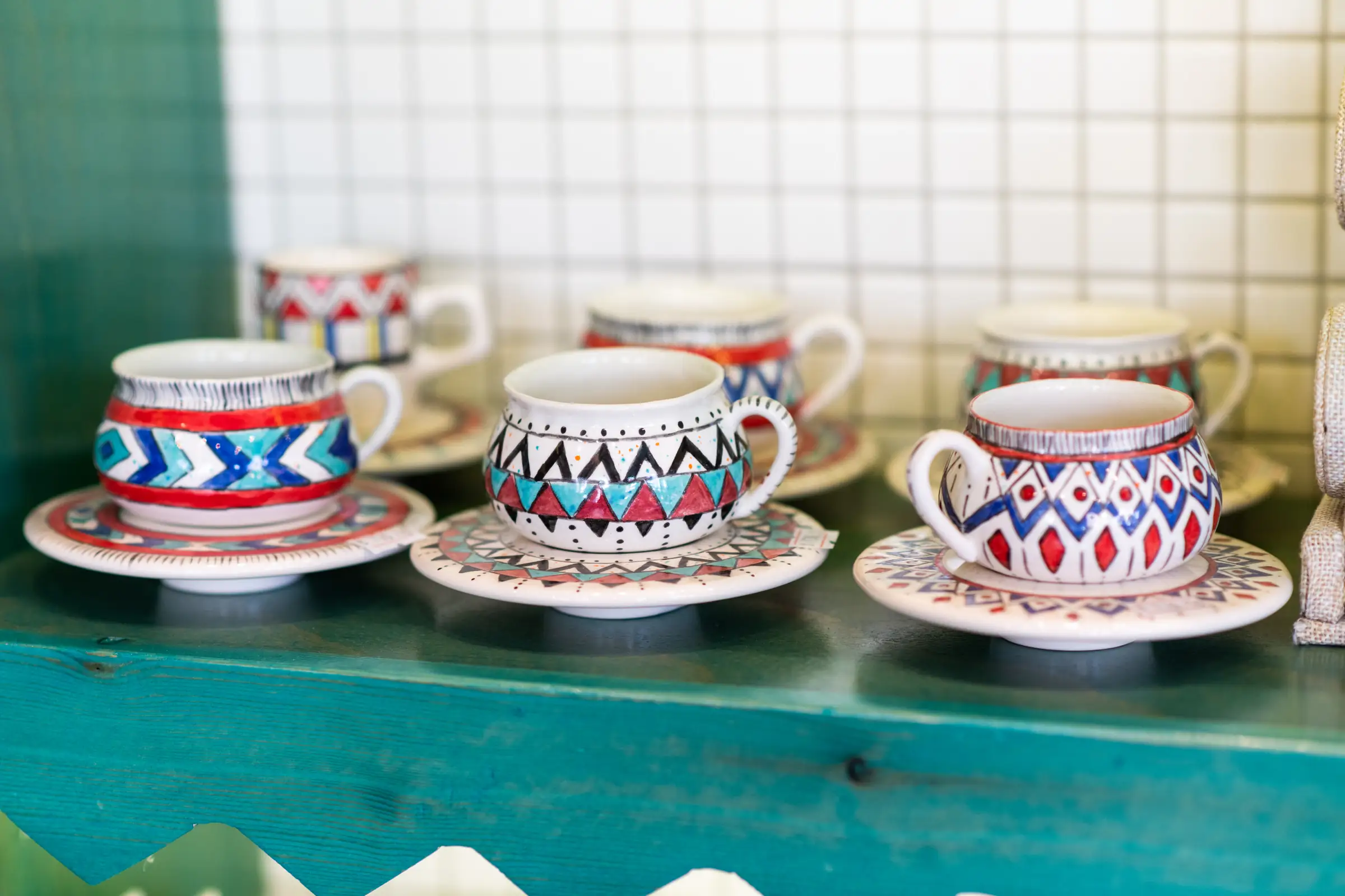 Hand painted espresso cups and saucers arranged on a turquoise shelf