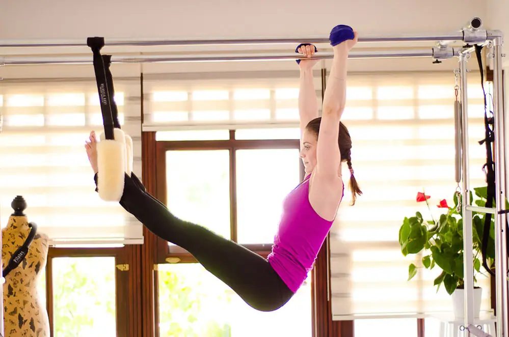 Woman holding a straight leg lift on the trapeze table against a bright window