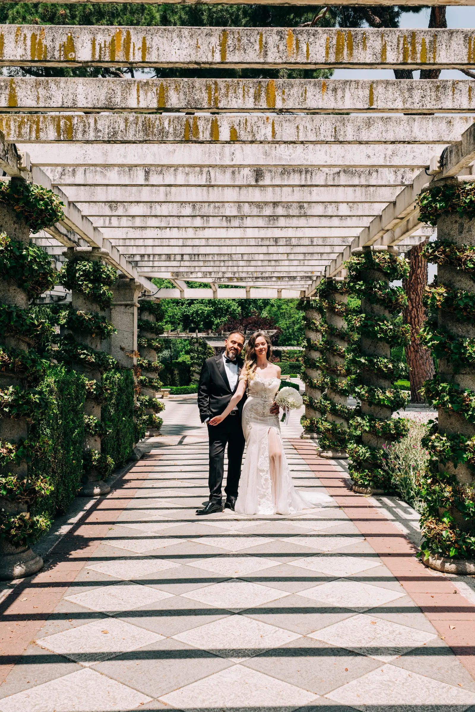 Bride and groom standing far down a wisteria pergola walkway in the Jardines de Cecilio Rodriguez, Madrid