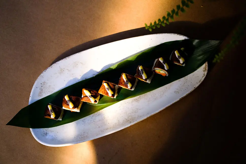Nigiri on a leaf lit by a single beam of light across a dark dish
