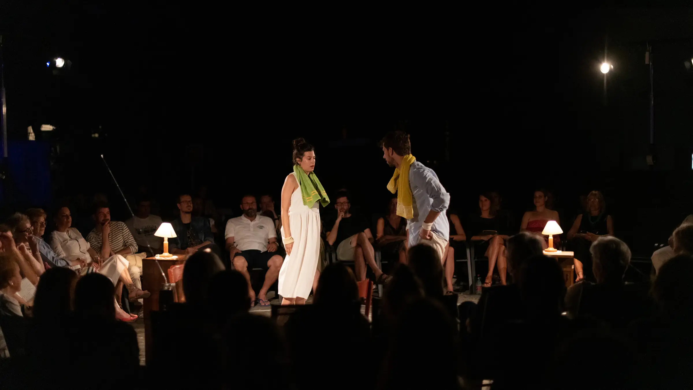 Two actors on a sand stage surrounded by the audience